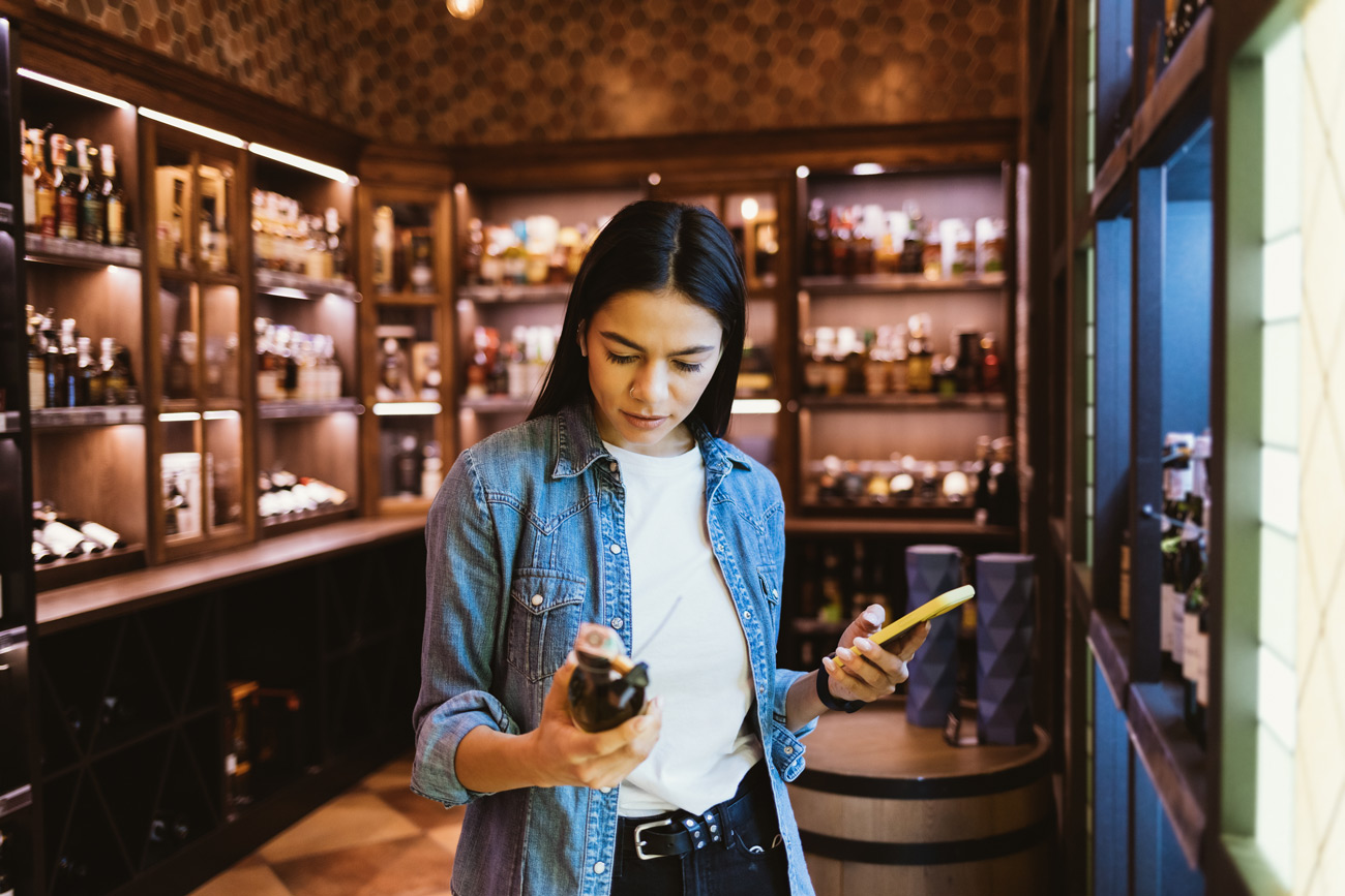 Woman deciding on which wine to buy in a shop with a conduct bond